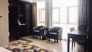A modern hotel room with a large window, a dark wooden wardrobe, two armchairs, a small table, and a dining table. - Zhongpu Hotel (Shangrao)