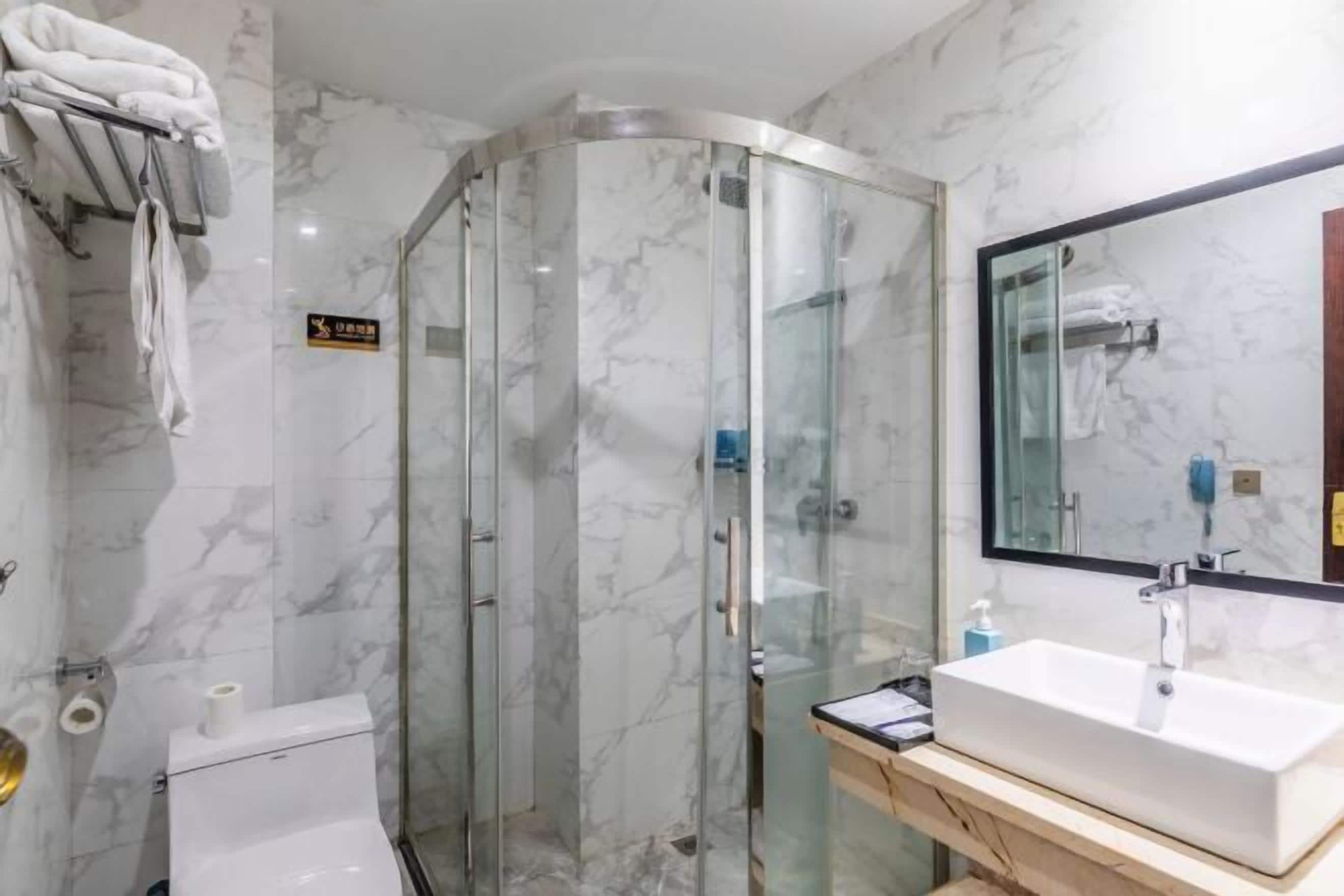 Un baño con cabina de ducha de vidrio, un lavabo blanco y pared revestida de mármol.