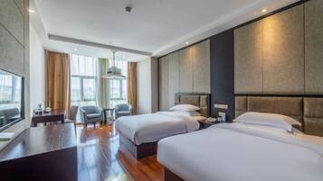 Habitación de hotel con dos camas, un escritorio, un televisor y un ventanal con cortinas.