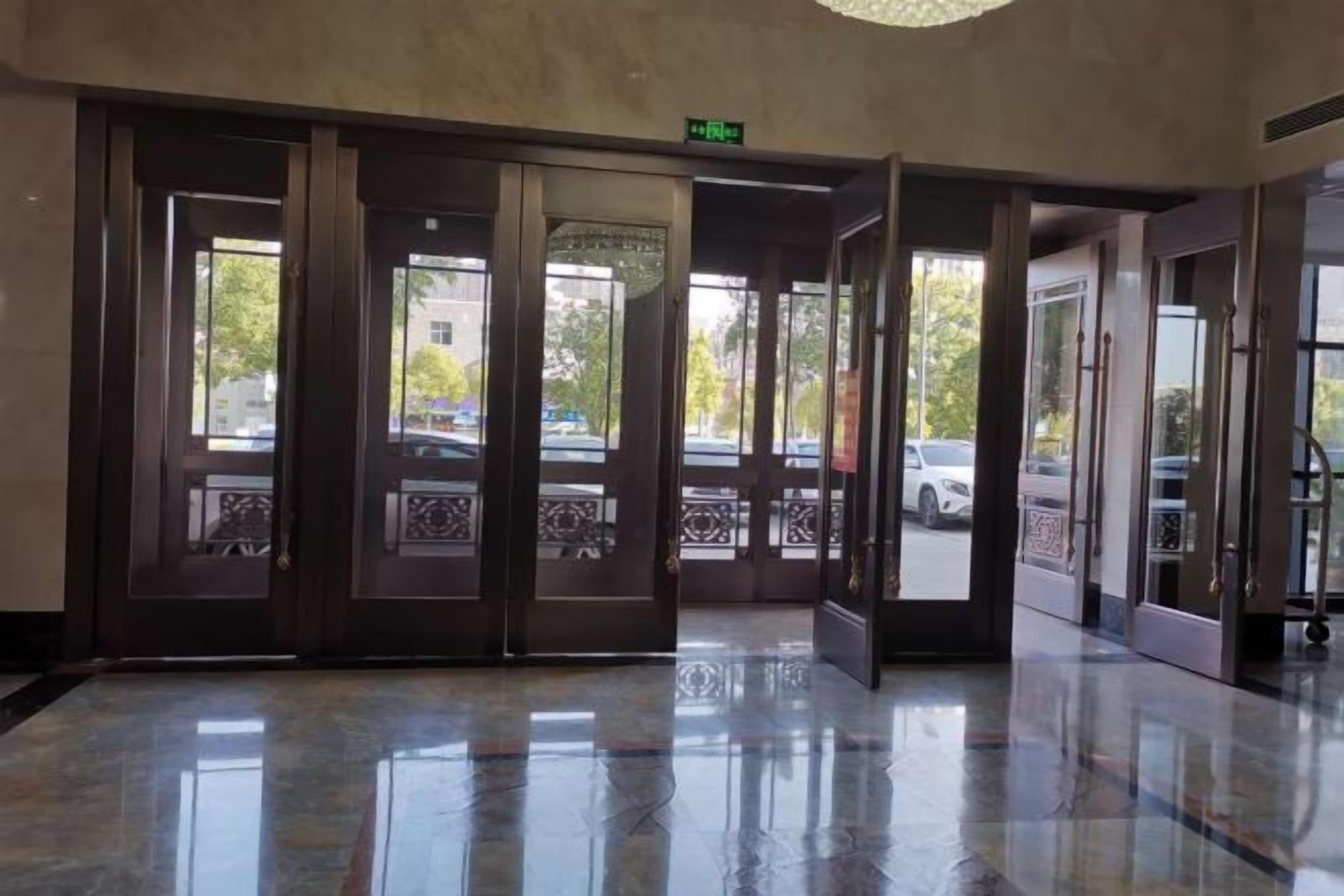 A hotel lobby with a marble floor, a set of revolving doors, and a view of the street outside.