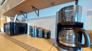 Eine Küche mit Kaffeemaschine, Mikrowelle und Behältern, beschriftet mit Kaffee und Zucker.