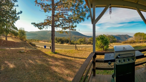 Überdachter Außenbereich mit Grill, Holzterrasse und Blick auf eine Straße und Hügel.