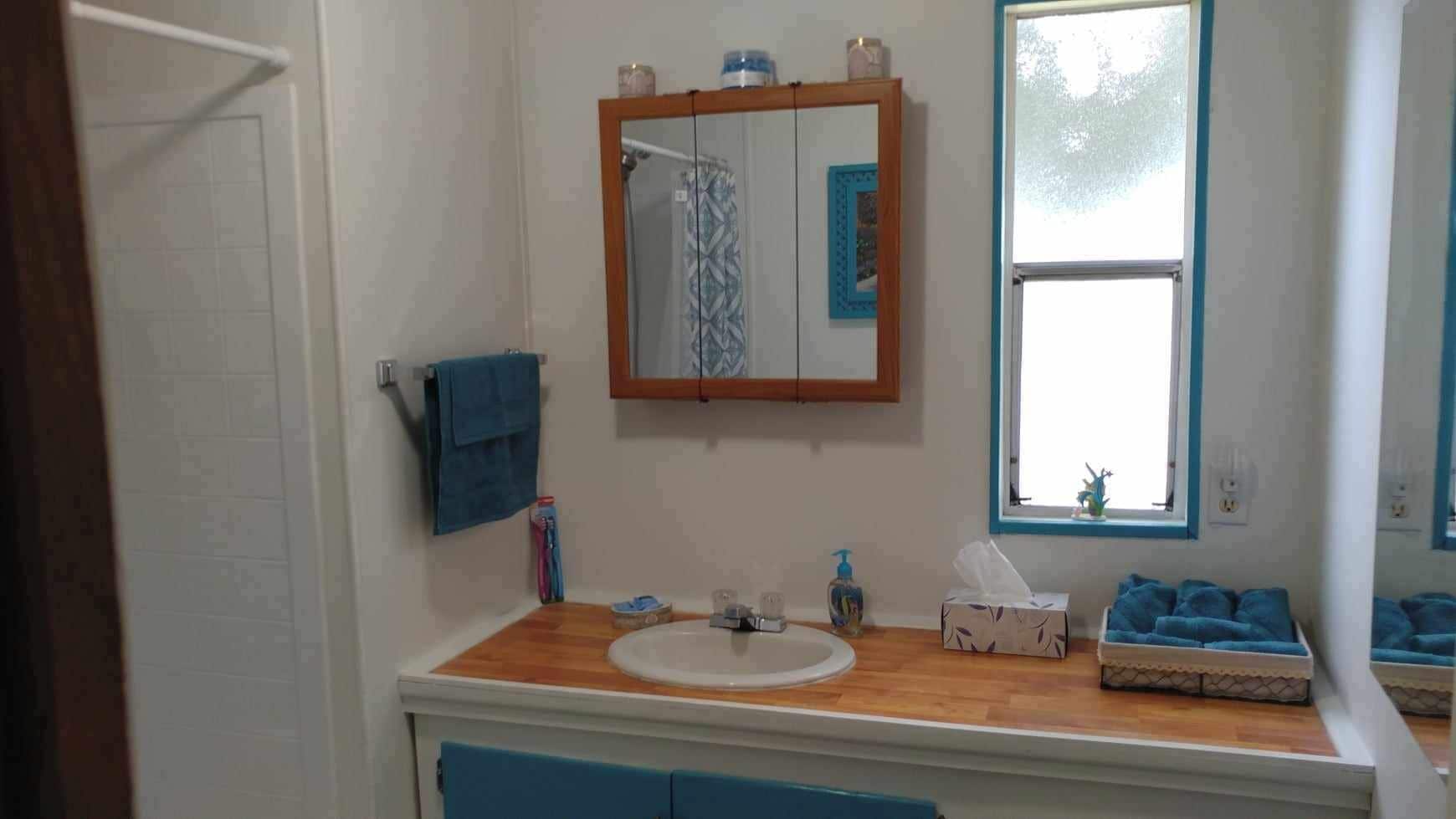 A bathroom with a wooden vanity, a white sink, a mirror, and a window.