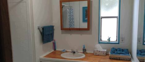 A bathroom with a wooden vanity, a white sink, a mirror, and a window.