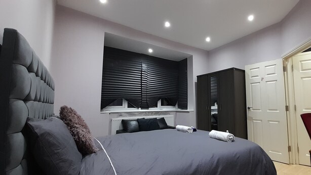 A modern bedroom with a large bed, a built-in wardrobe, and a dining area with a table and chairs. - Privet apartment with 2 bedrooms for relaxing escape in EastHam near CentralPark (London)