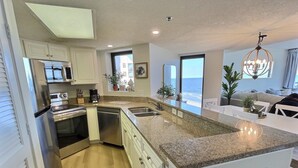 A modern kitchen with a large island, stainless steel appliances, and a view of the ocean. - Oceanfront Escape! Stylish 3 bedroom corner unit (North Myrtle Beach)