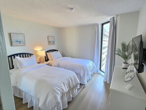 A hotel room with two beds, a desk with a TV, and a window with curtains. - Oceanfront Escape! Stylish 3 bedroom corner unit (North Myrtle Beach)