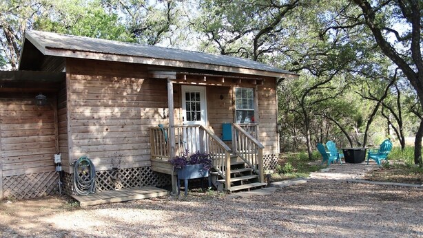 A wooden cabin with a porch, outdoor seating, and a gravel ground. - Austin Cabin (Austin)