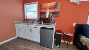 A compact kitchen with white cabinets, a dishwasher, and a window with blinds. - Austin Cabin (Austin)