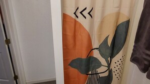 A bathroom with a shower curtain featuring a leaf design, a dark rug, and a towel hanging on the wall. - Austin Cabin (Austin)