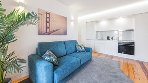 Ein modernes Wohnzimmer mit einem blauen Sofa, eine Küche mit weißen Schränken und ein großes Gemälde der Golden Gate Bridge.