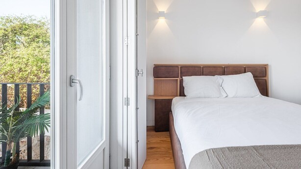 Ein Schlafzimmer mit Bett, Nachttisch, Holz-Kopfteil und Balkon mit Pflanze.