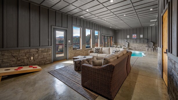 A spacious indoor area with a large sofa, a coffee table, and a ping pong table. There are multiple windows offering views of the outdoors. - Beautiful Mt. View Pool Cabin with Hot Tub & Arcade Games! Perfect for Families! (Sevierville)
