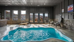 An indoor swimming pool with a view of autumn trees, stone walls, and a lifeguard sign. - Beautiful Mt. View Pool Cabin with Hot Tub & Arcade Games! Perfect for Families! (Sevierville)