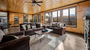 A spacious living room with wooden ceilings and large windows offering a view of the outdoors. - Beautiful Mt. View Pool Cabin with Hot Tub & Arcade Games! Perfect for Families! (Sevierville)