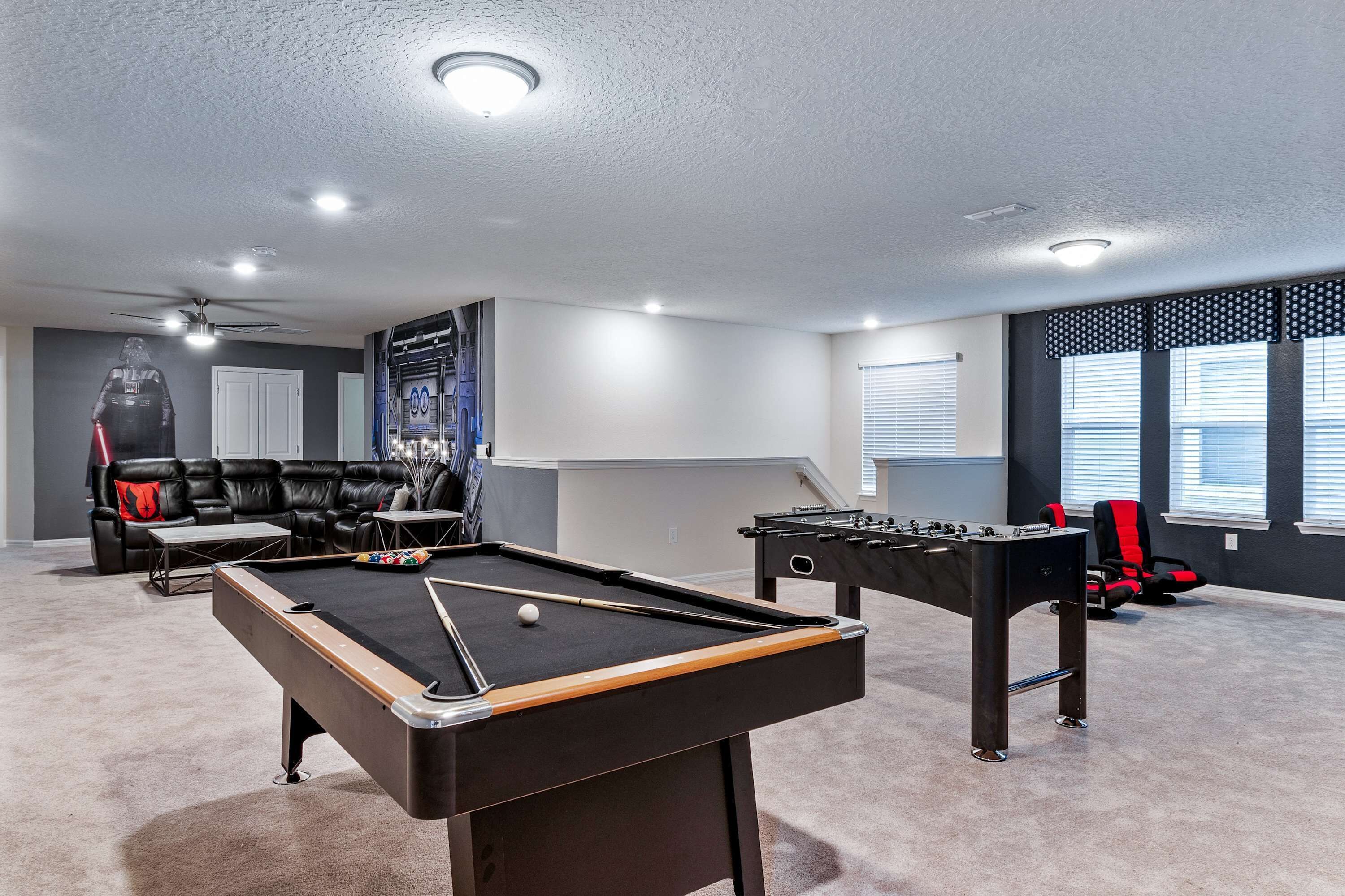 Une pièce avec une table de billard, un baby-foot, un canapé et une grande affiche au mur.