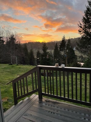 A wooden deck with a railing overlooking a grassy area and a forested landscape.