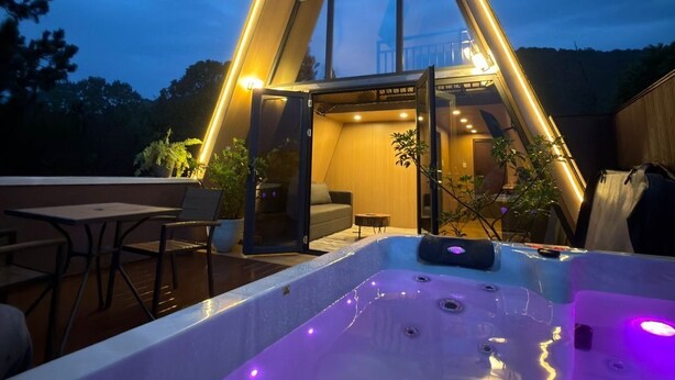 Un bâtiment moderne doté d’un toit triangulaire, d’un jacuzzi et d’un espace patio aménagé avec des sièges.