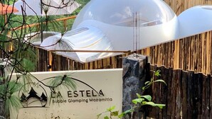 Une enseigne indiquant « A ESTELA Bubble Glamping Mazamitla », avec une clôture en bois et un ciel dégagé en arrière-plan.