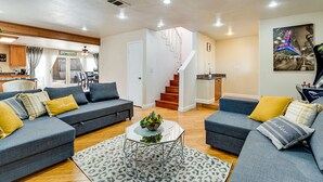 Un salón espacioso con dos sofás grises, una mesa de centro y una escalera que sube a un piso superior.