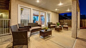 Un patio al aire libre con mobiliario de mimbre, una mesa de centro de vidrio y vistas a la calle.