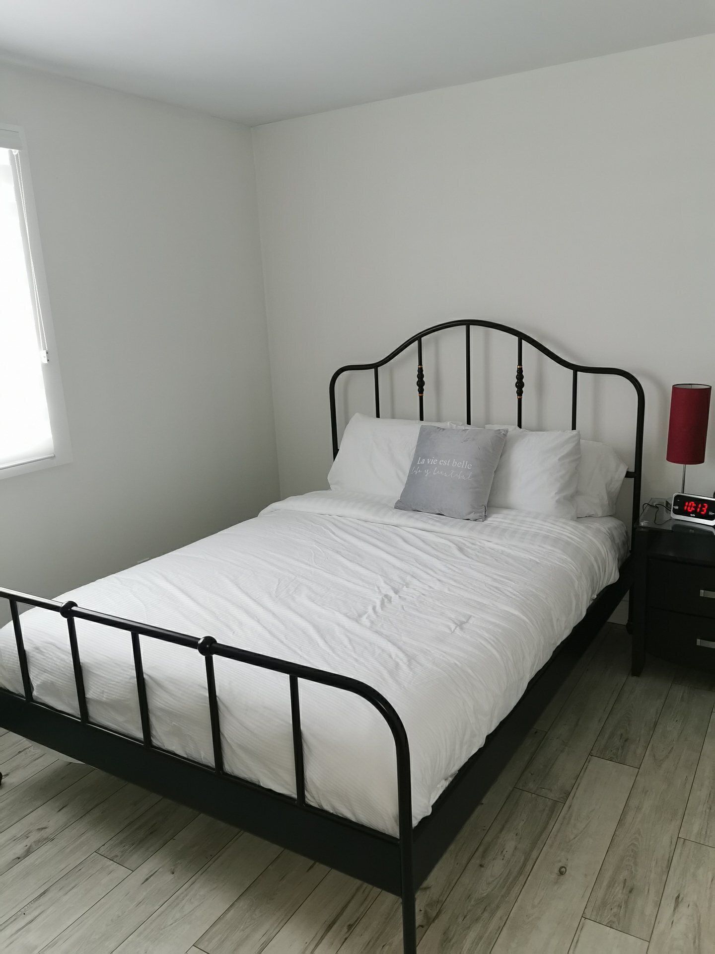 Ein Einzelbett mit schwarzem Metallgestell, weißer Bettwäsche und einem Nachttisch mit einer roten Lampe.