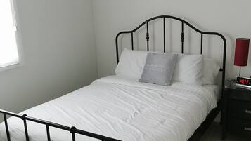 Ein Einzelbett mit schwarzem Metallgestell, weißer Bettwäsche und einem Nachttisch mit einer roten Lampe.