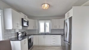 A modern kitchen with white cabinets, a stainless steel refrigerator, and a built-in oven.
