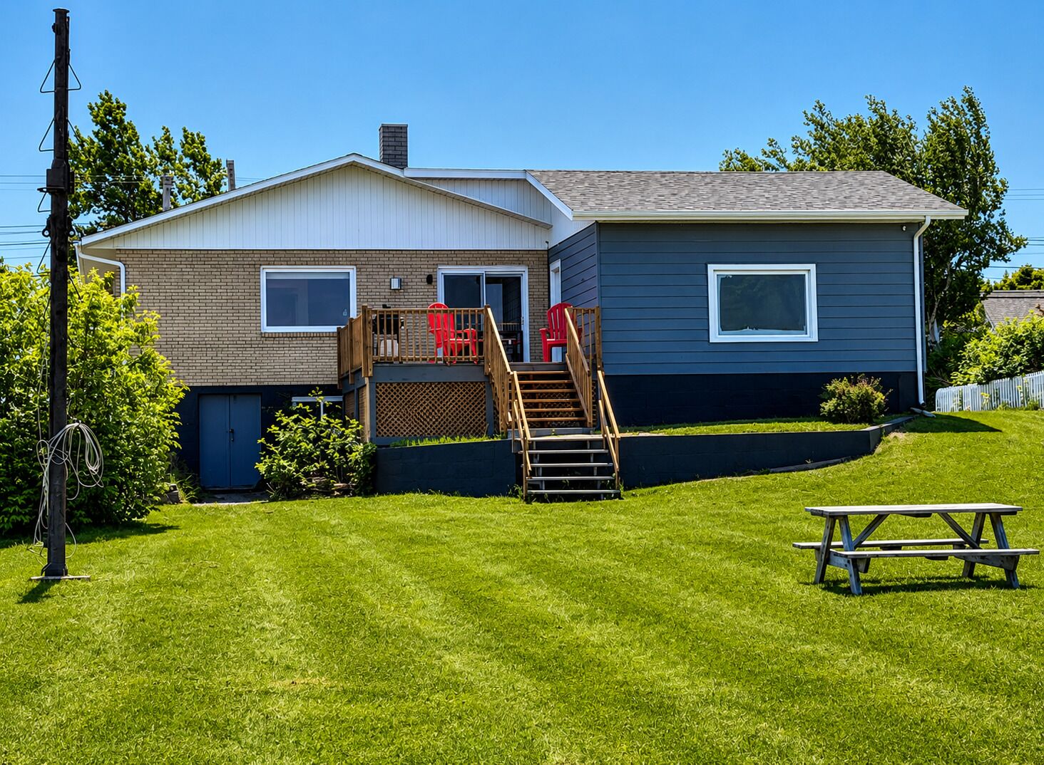 A two-story house with a front deck, a staircase, and a picnic table in the yard.