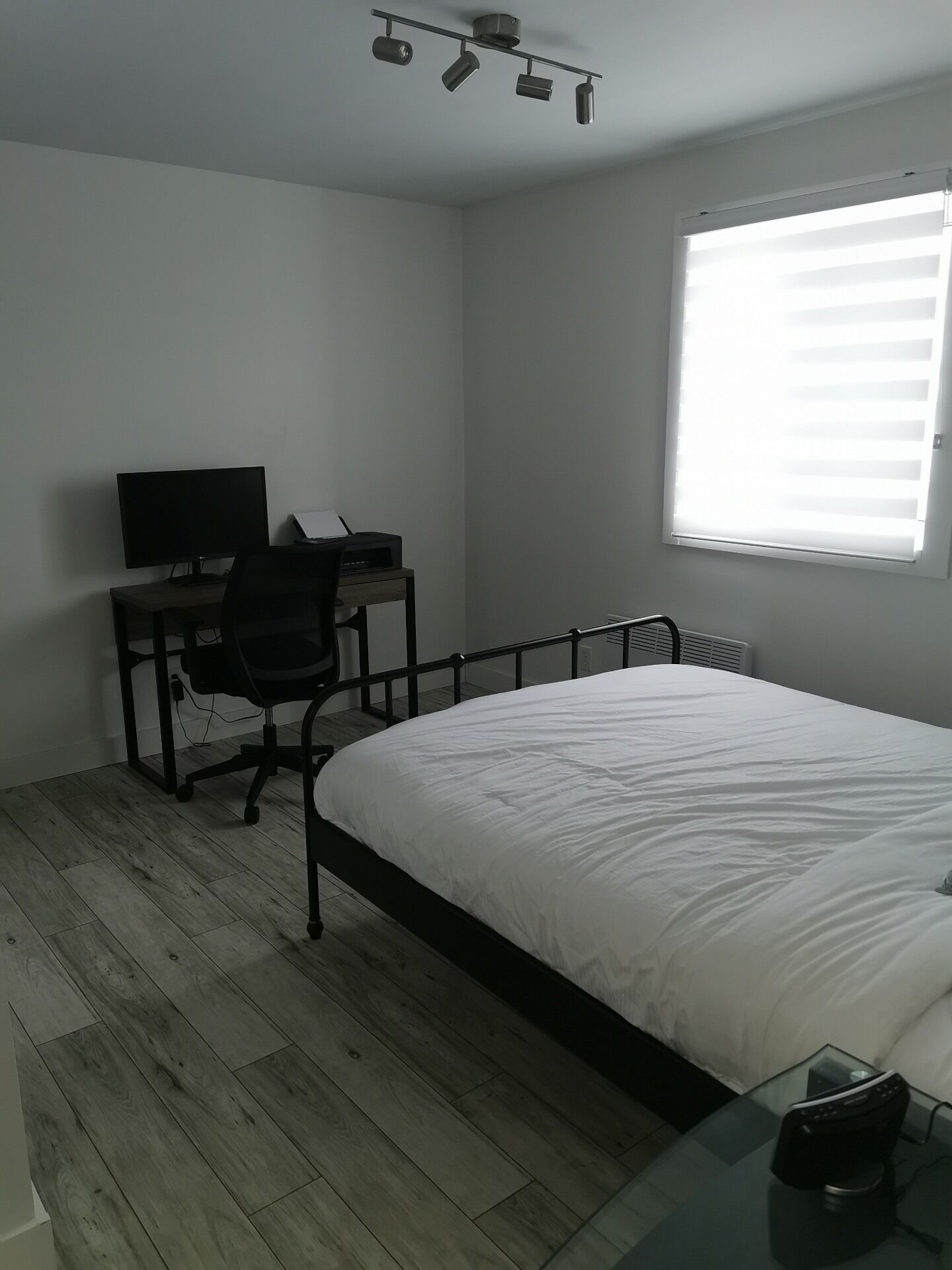 Une chambre à coucher avec un lit, un bureau avec un ordinateur, une chaise et une fenêtre avec des stores.