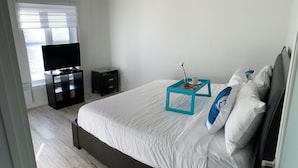 A bedroom with a large bed, a TV, a small table with a tray, and a window with blinds.
