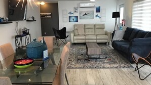 A modern living room with a glass dining table, a beige sofa, a blue sofa, and a coffee table.