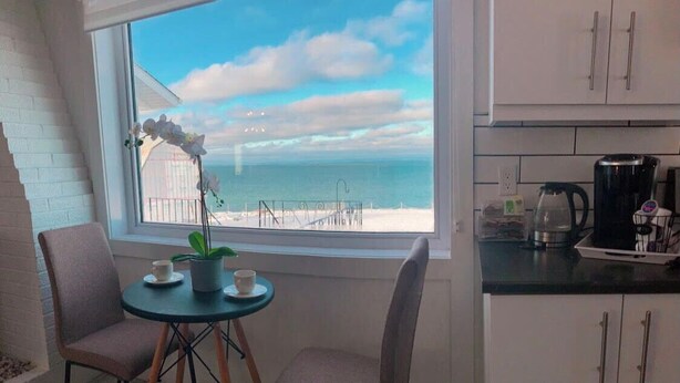 A small kitchen with a view of the beach, two chairs, a table with cups, and a potted plant.