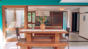 A dining area with a wooden table and chairs, a vase with flowers, and a view of the outdoors through large glass doors.