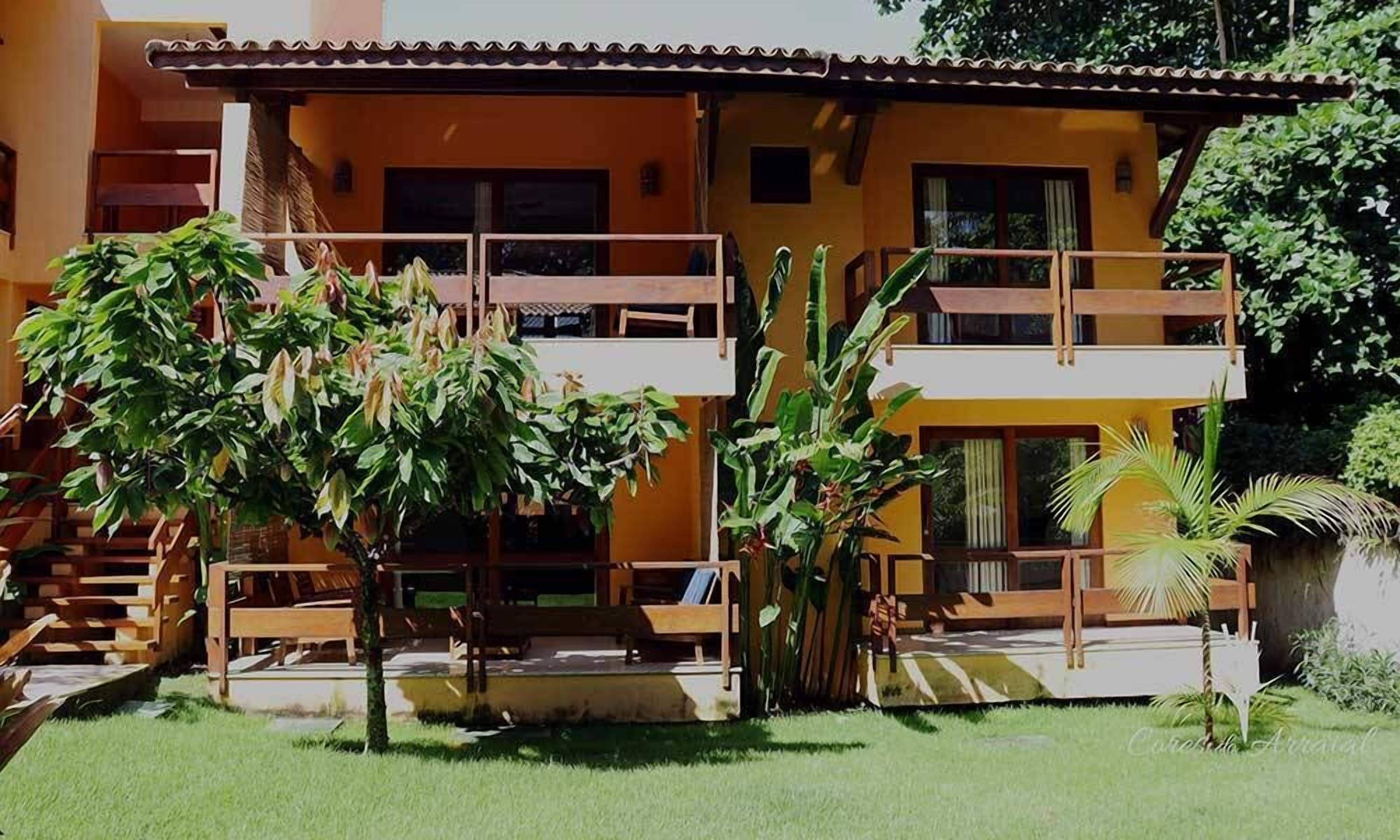 A two-story building with a balcony, surrounded by greenery and a small pool area.