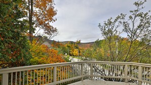 A wooden deck with a railing overlooking a forested area with autumn foliage. - Paging Dr. Powder Condo with Mountain Views on Shuttle Route (Killington)