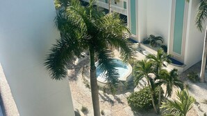 Une cour d’hôtel agrémentée de palmiers, une piscine et, au fond, un immeuble à plusieurs étages.