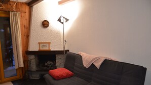 A cozy living room with a dark grey sofa, red cushions, a fireplace, and a standing floor lamp. - flat for rent in Les Collons (Thyon-Les Collons)