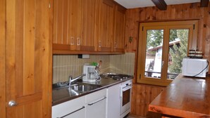 A kitchen with wooden cabinets, a white dishwasher, and a window with a view of trees. - flat for rent in Les Collons (Thyon-Les Collons)