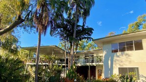 A two-story house with a covered patio, surrounded by lush greenery and palm trees.