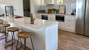 A modern kitchen with a large island, bar stools, stainless steel appliances, and a view of the outdoors.