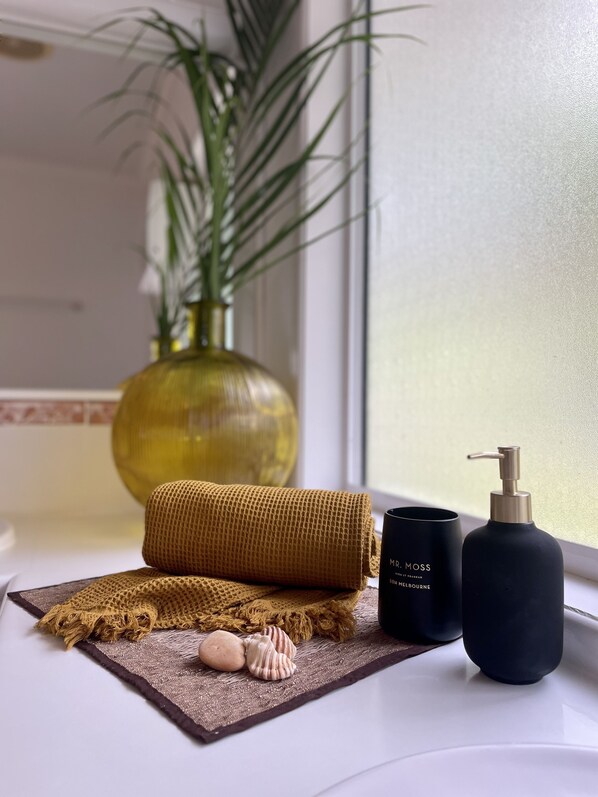 Un meuble-lavabo de salle de bain avec une serviette, une bouteille de gel douche de la marque Mr. Moss et un vase avec une plante.