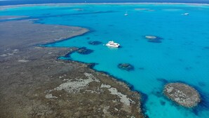 An aerial view of a coastal area with clear turquoise waters, a boat, and rocky terrain.