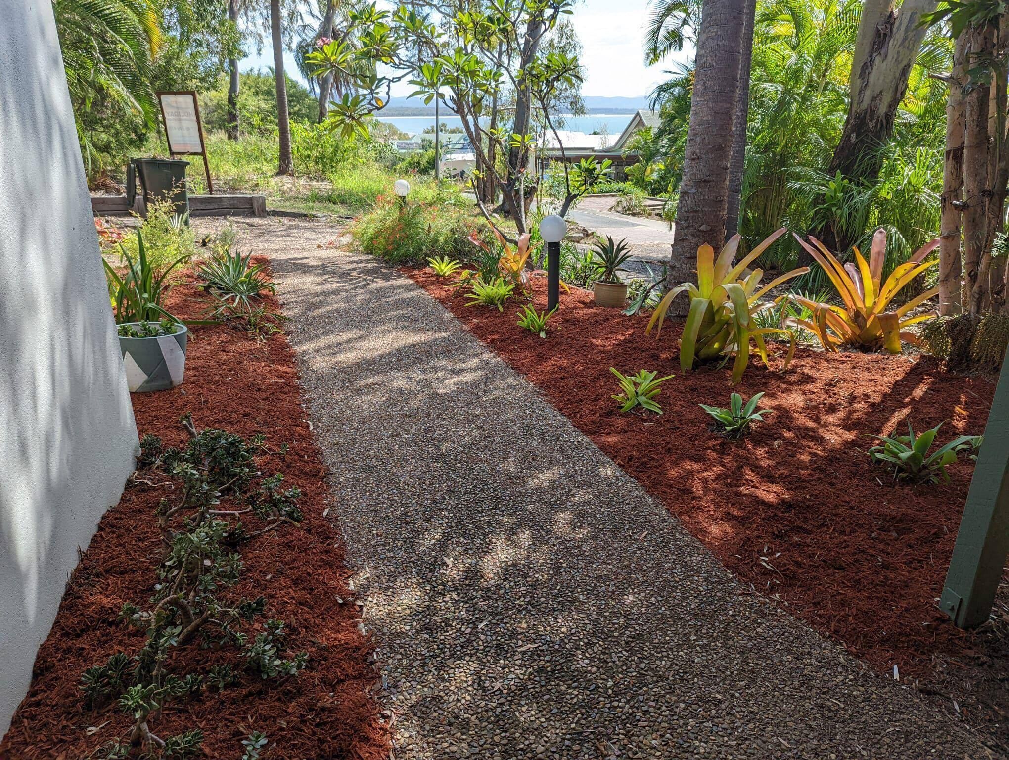 A pathway leading to a beach with a view of the ocean, surrounded by tropical plants and trees.