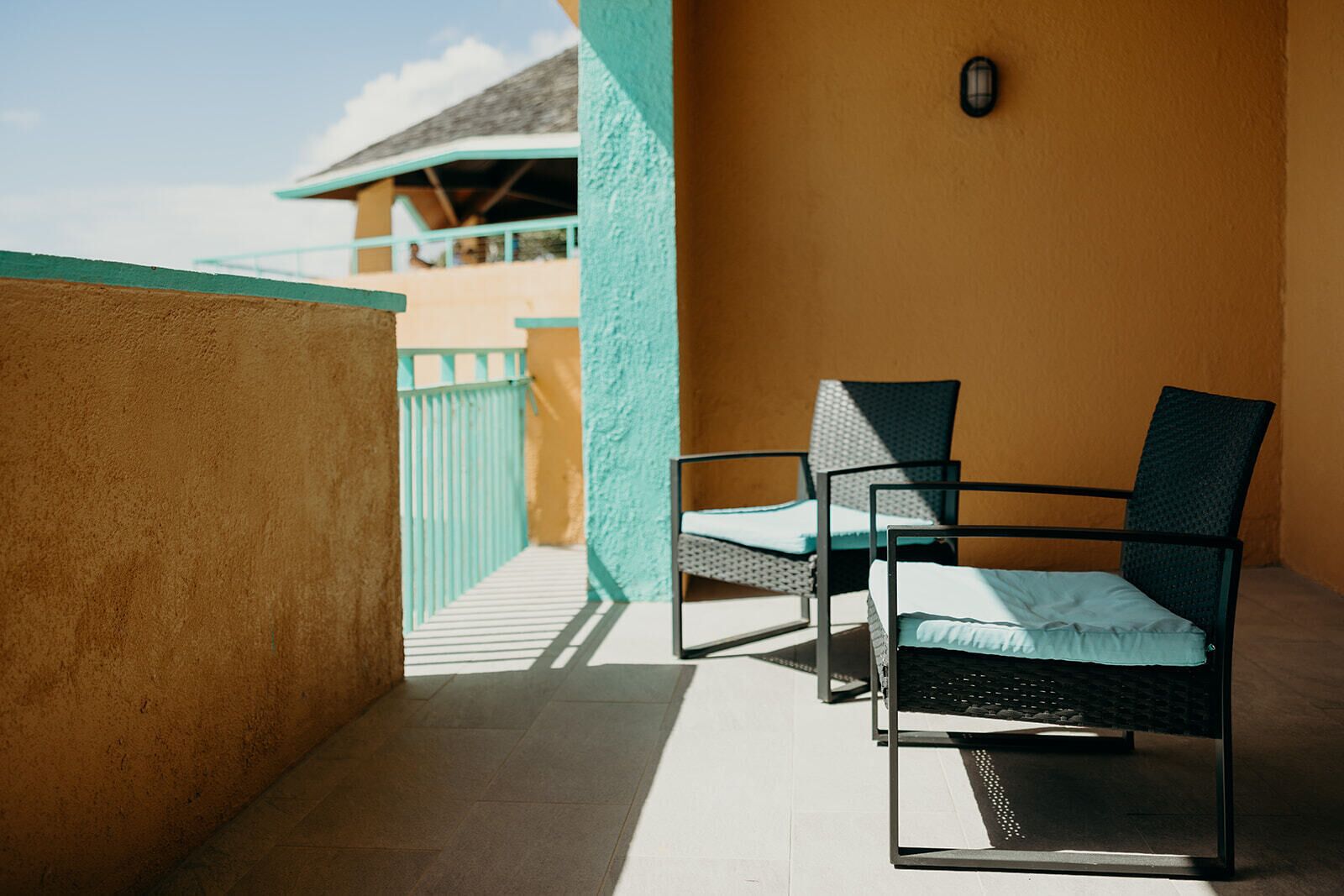 A balcony with two chairs and a view of a building with a turquoise roof.