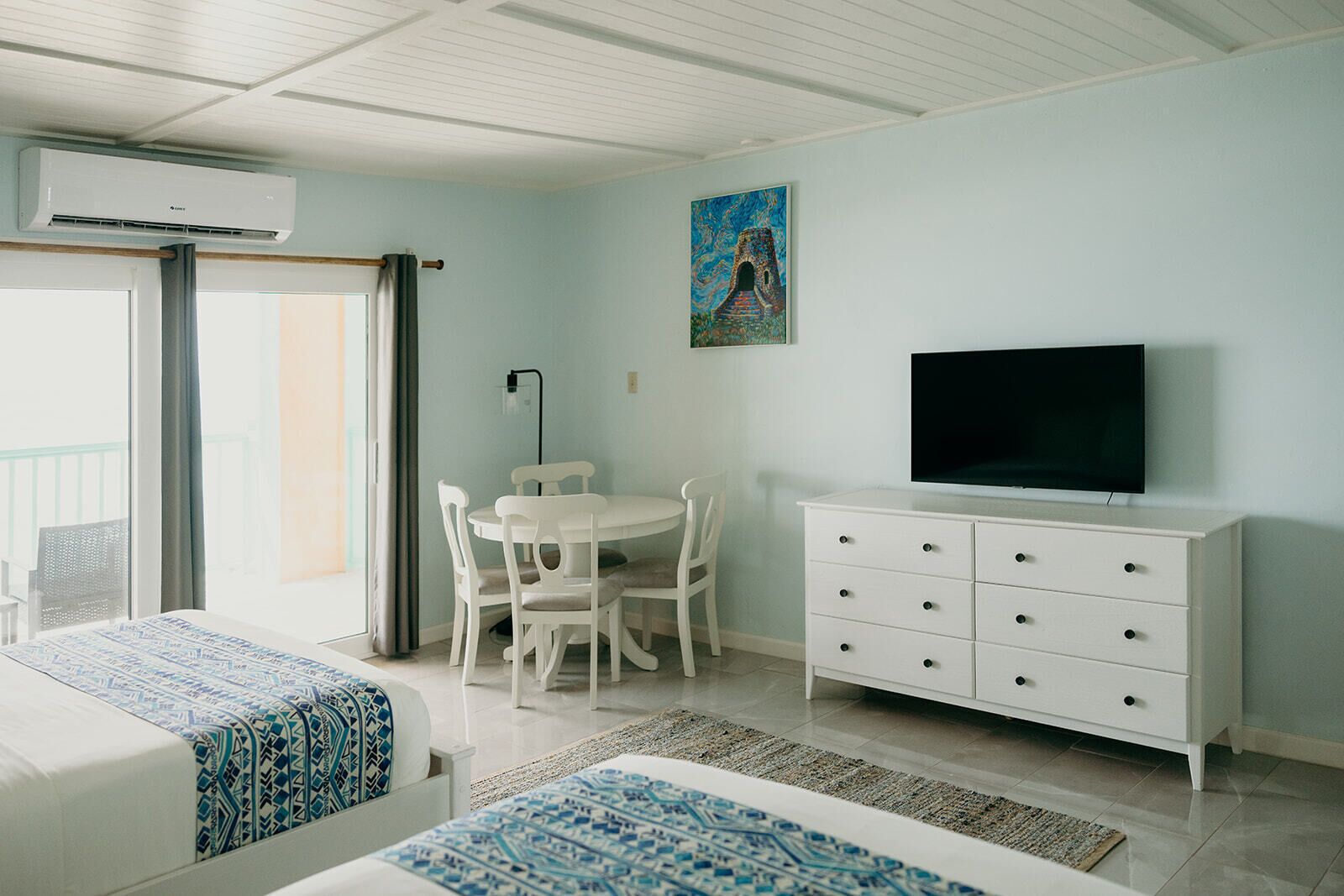 Ein Hotelzimmer mit Bett, Esstisch mit Stühlen, Fernseher auf einer Kommode und einem Bild an der Wand.