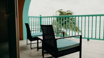 A balcony with two black chairs and a table, a teal railing, and a view of palm trees.