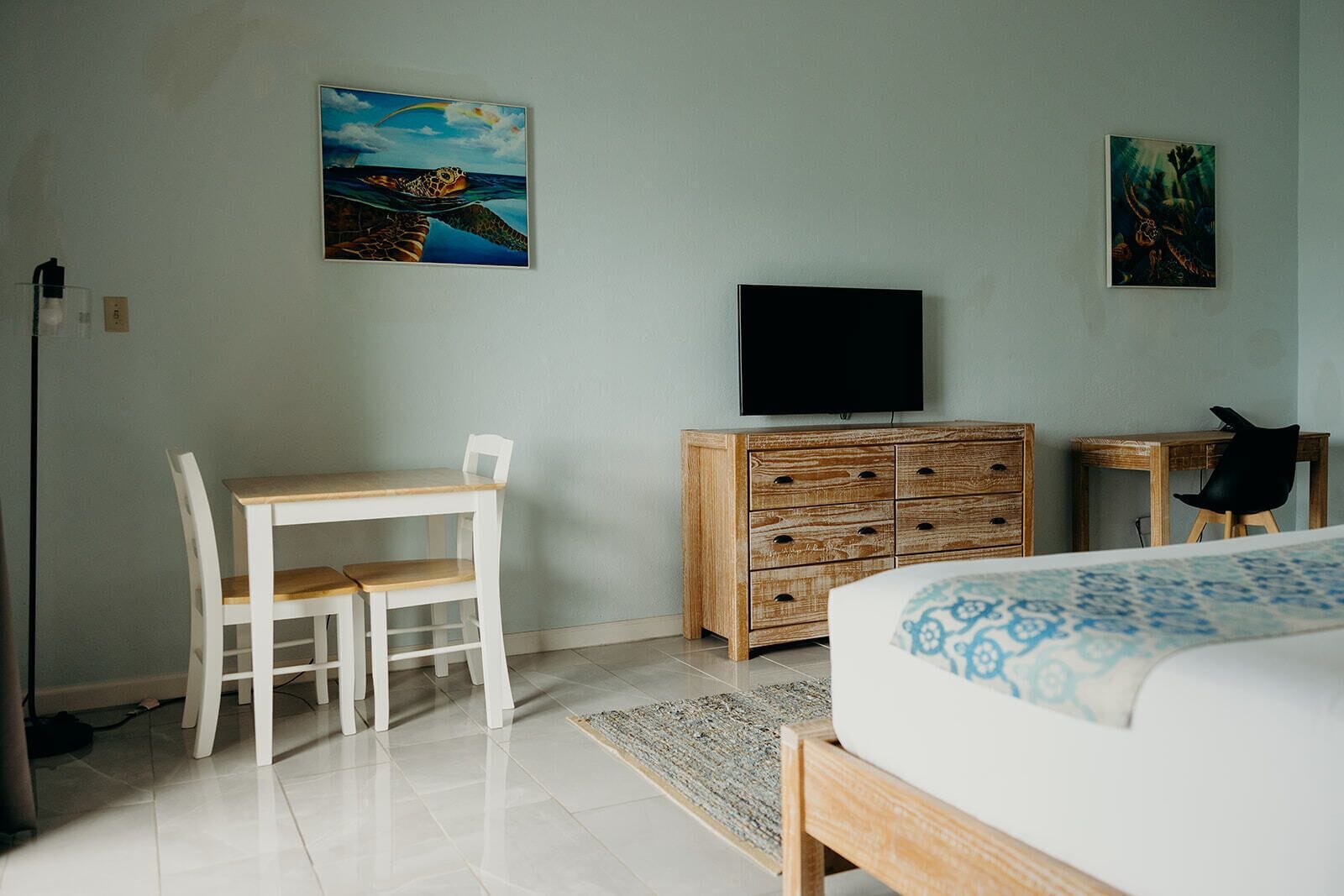 Une chambre à coucher avec un lit, un bureau avec des chaises, une commode et un téléviseur fixé au mur.