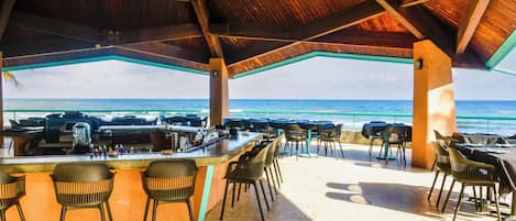 Un espace bar extérieur abrité, avec vue sur l’océan, des tabourets de bar et un barbecue.