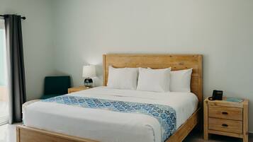 A neatly made bed with a patterned bedspread, a bedside table with a lamp, and a nightstand with a phone.